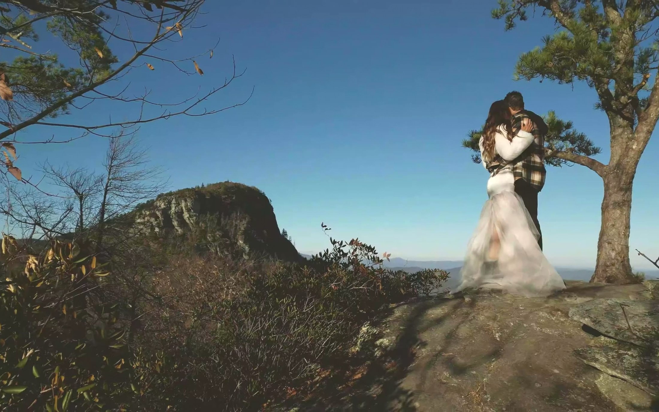 Elopement couple standing small on a Blue Ridge mountain overlook at golden hour in western North Carolina