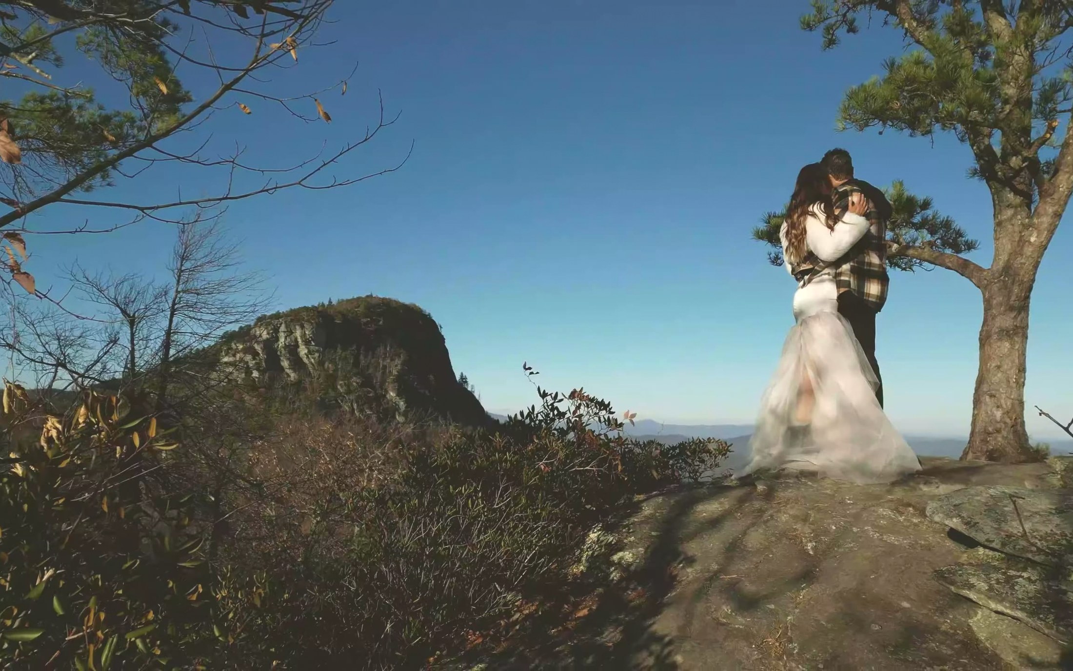 Elopement couple standing small on a Blue Ridge mountain overlook at golden hour in western North Carolina
